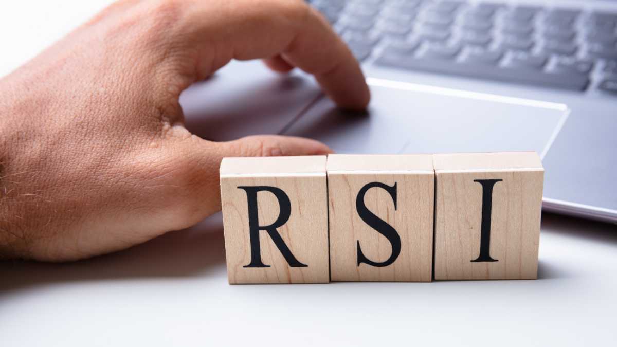 Hand aligning wooden blocks with the letters RSI on a desk near a laptop