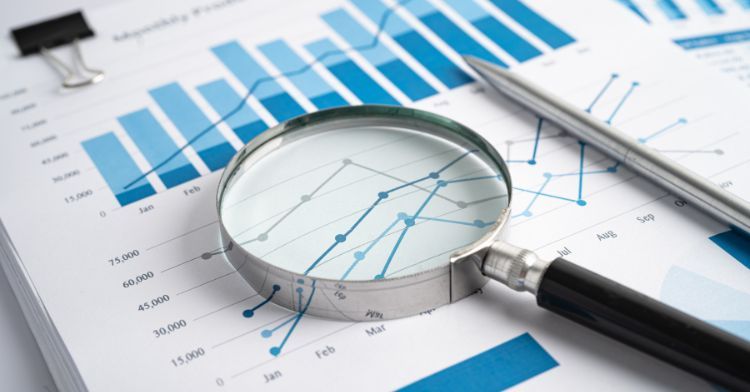 A close-up of a magnifying glass focusing on a financial chart with blue graphs and figures.