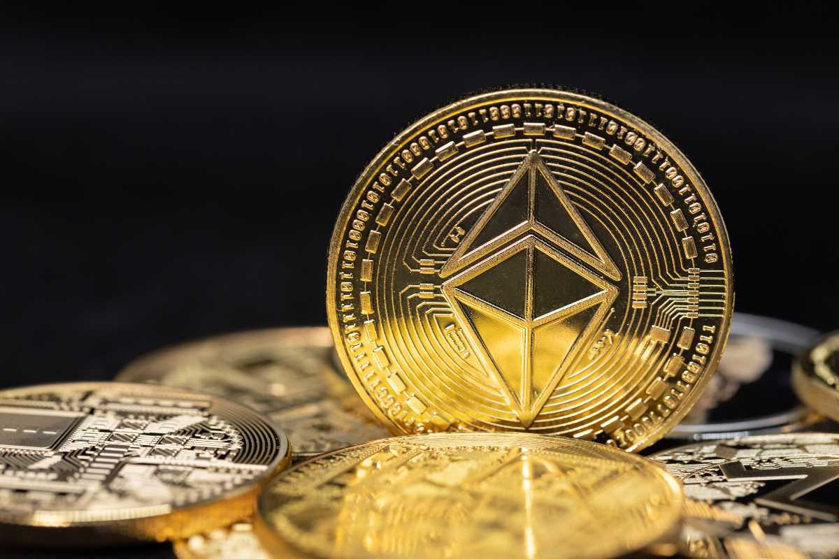 A collection of golden Ethereum coins piled on a dark surface, with the Ethereum logo visible.