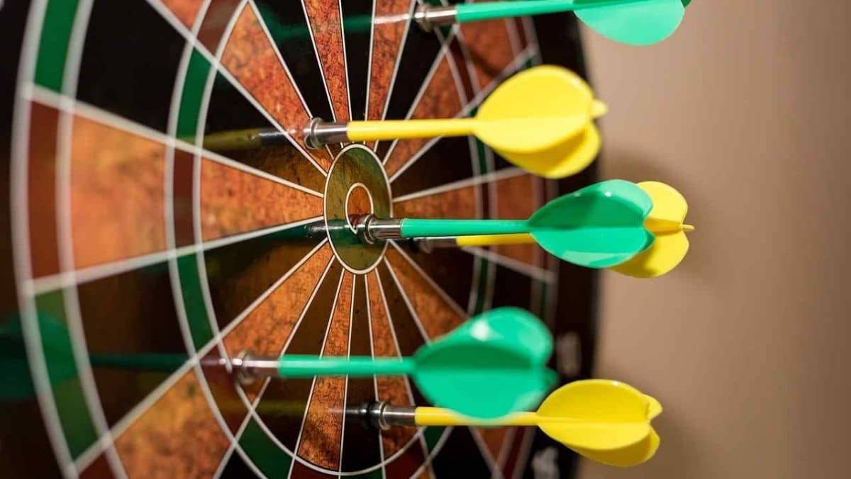 A dart lodged in the center of the board amid others scattered around