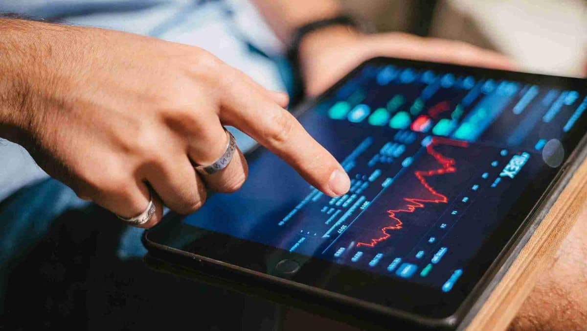 A fingertip touches the screen of a table showcasing a trading chart