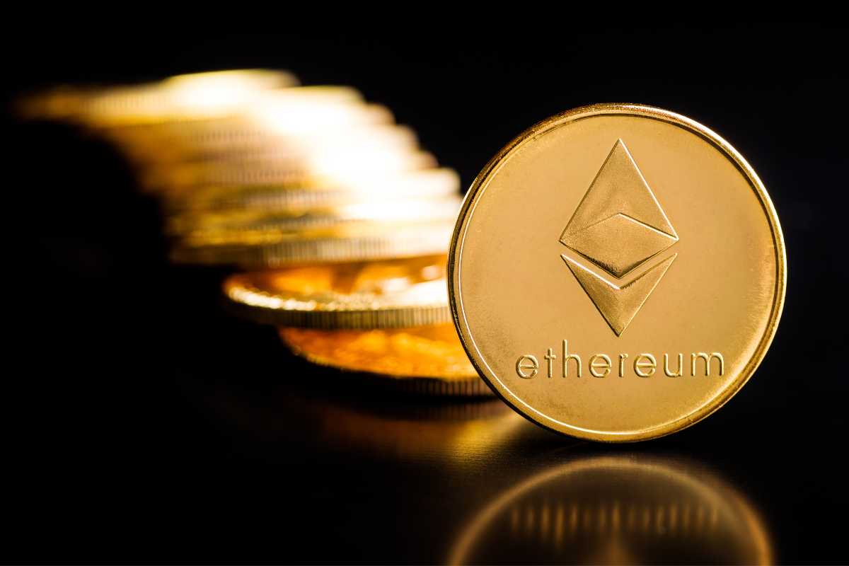 A golden Ethereum coin in focus with a blurred stack of coins in the background