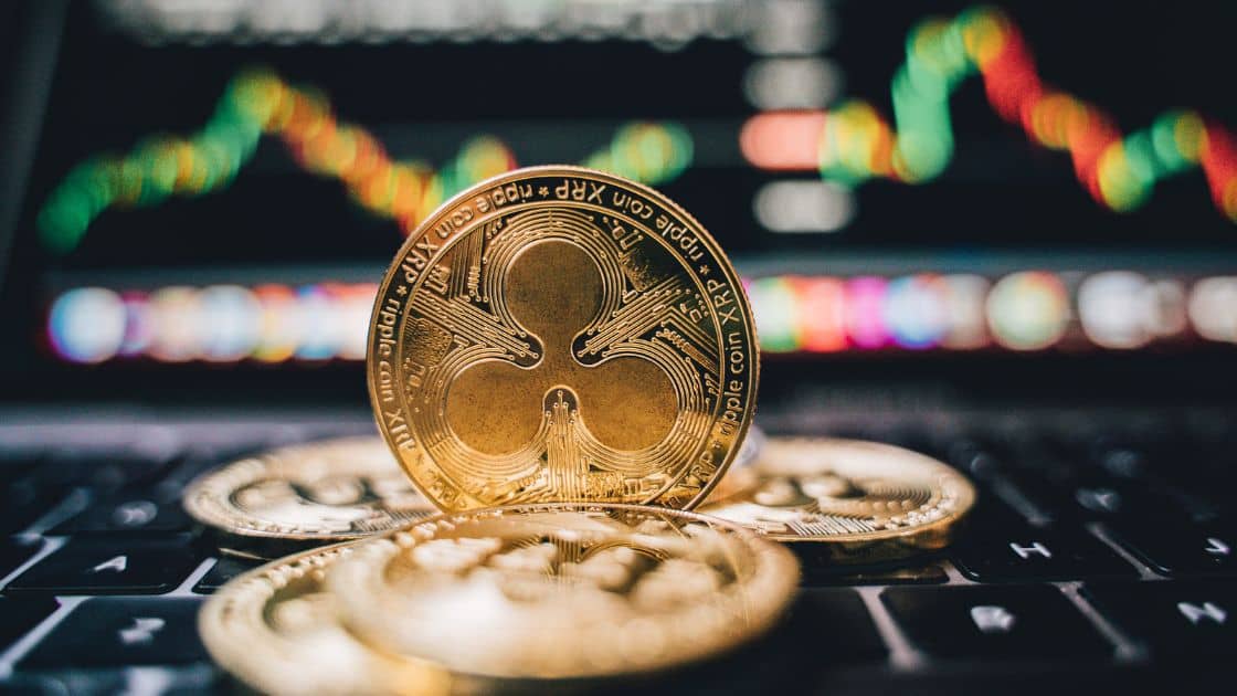 A golden Ripple XRP cryptocurrency coin centred on a laptop keyboard with colourful trading graph reflections on the screen