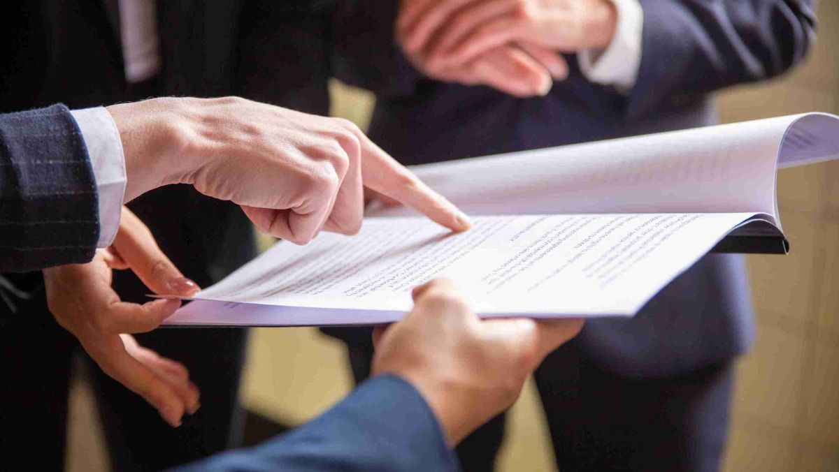 A hand gesturing towards a paper document surrounded by people in the background