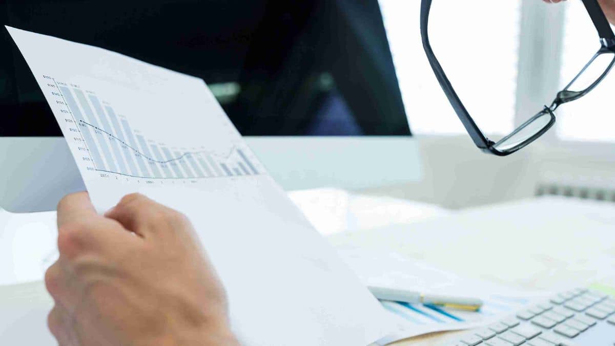 A hand holding a paper with bar graphs while the other hand grasps eyeglasses