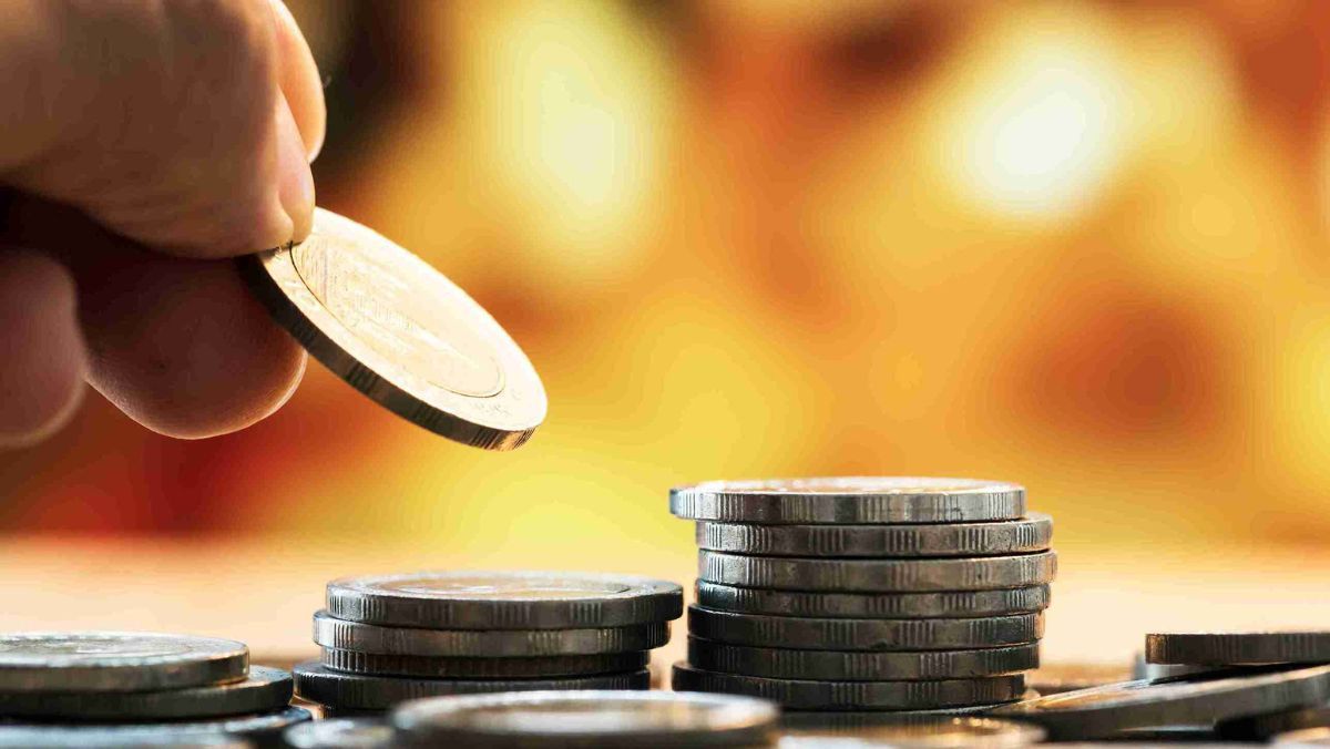 A hand placing a coin onto a collection of scattered coins on a flat table