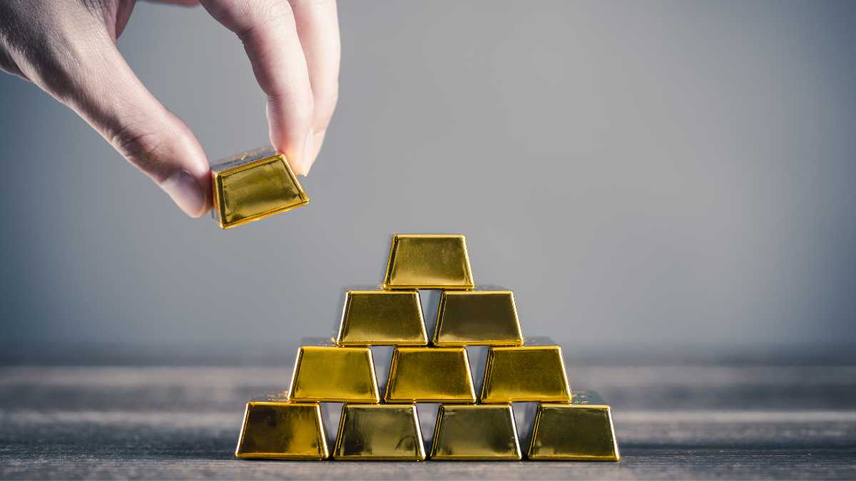 A hand placing a gold bar on a pyramid made of gold bars
