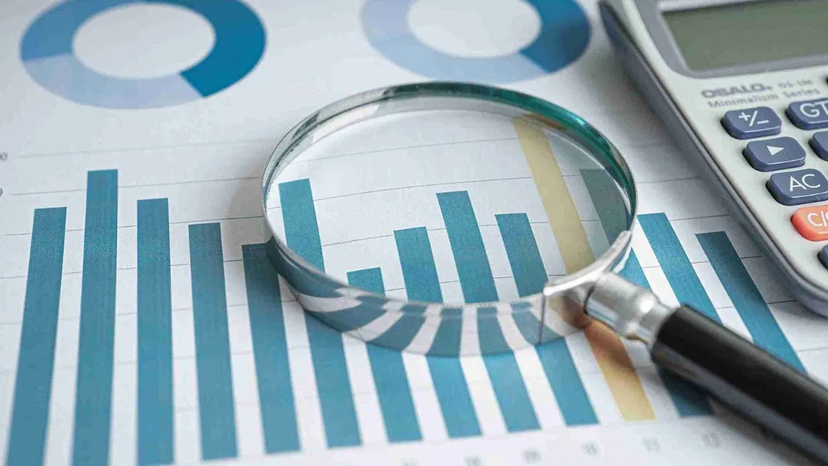 A magnifying glass positioned on charts and graphs, accompanied by a calculator placed on the desk
