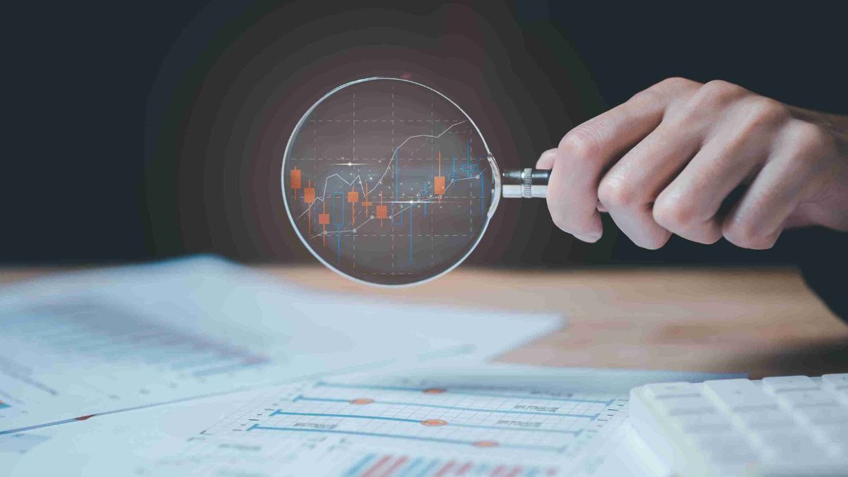 A magnifying glass reveals trading patterns on its lens with financial documents scattered on the table
