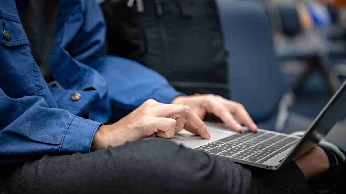 A man in blue attire using a laptop placed on his crossed legs