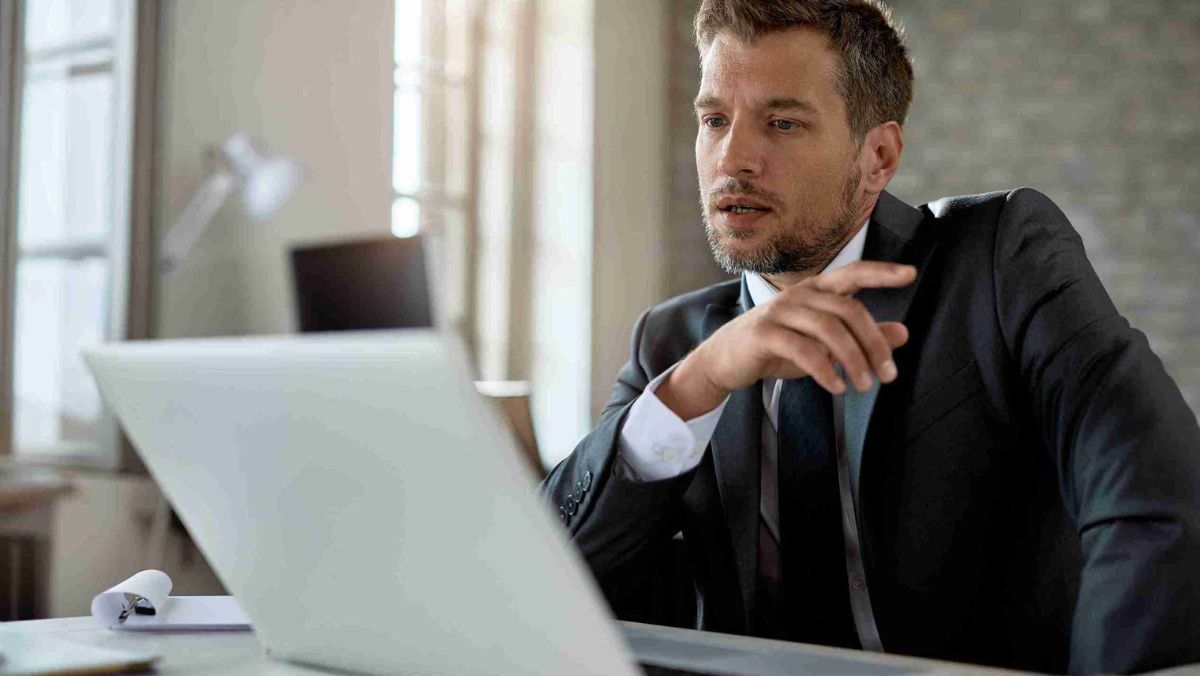 A man in formal attire diligently working in an office setting with a laptop