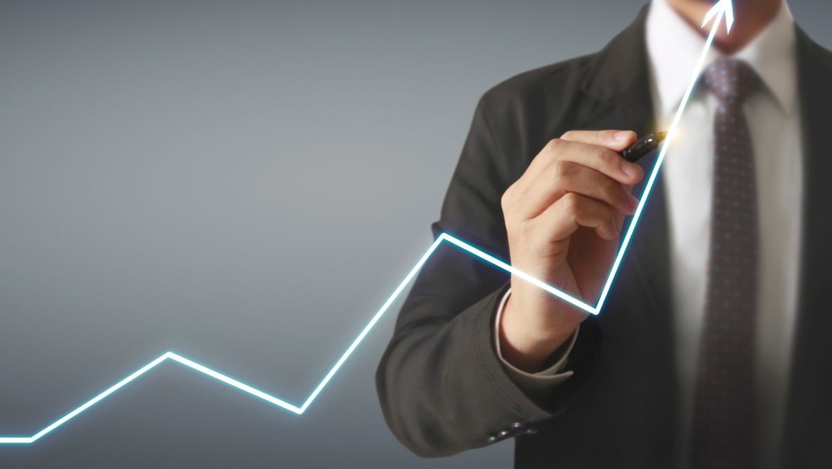 A man in formal attire pointing an upward direction of a white arrow using a pen