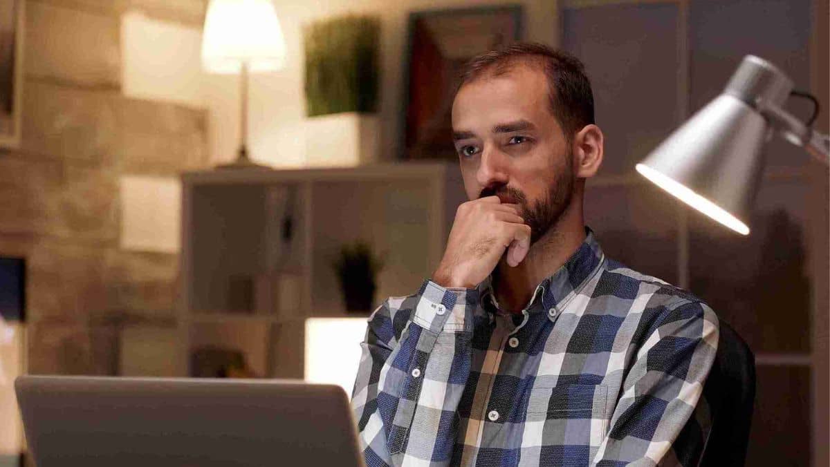 A man in his office deeply immersed in thought while seated in front of his computer