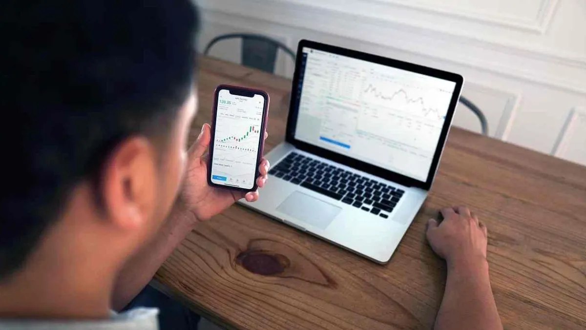 A man is holding a mobile phone while a laptop rests on the table