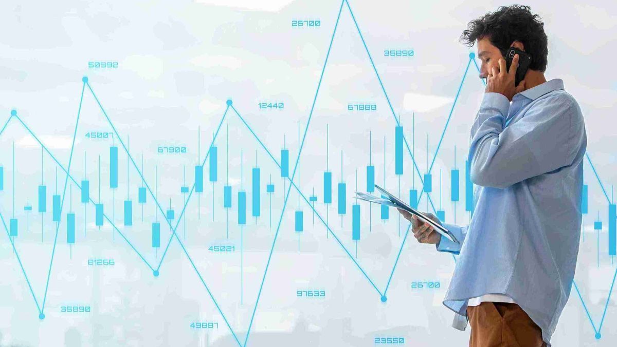 A man reviewing documents while talking on the phone, surrounded by blue colored trading charts