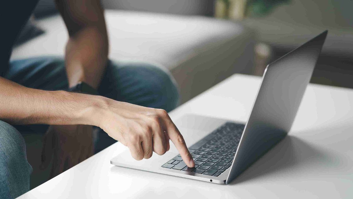 A man tapping a key on the laptop keyboard resting on the table