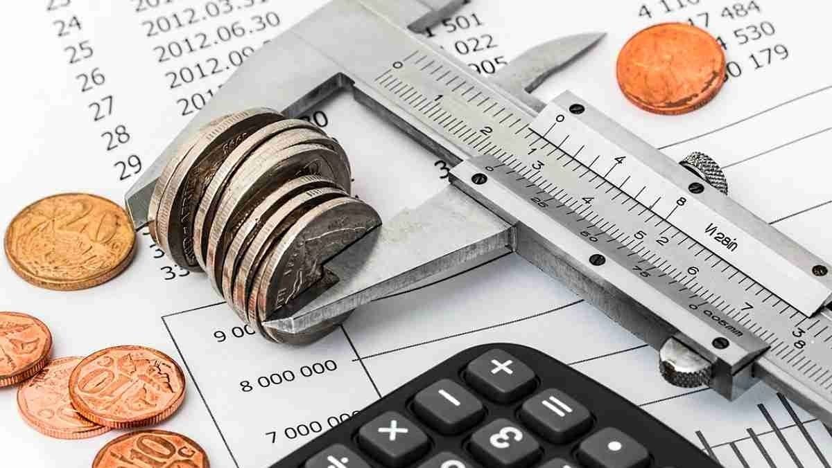 A measuring tool gauging the thickness of a pile of coins next to a calculator
