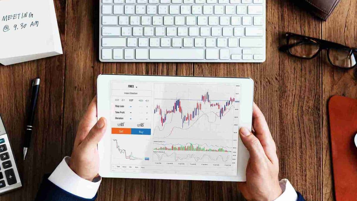A person at a desk engaged in studying forex charts on a tablet device