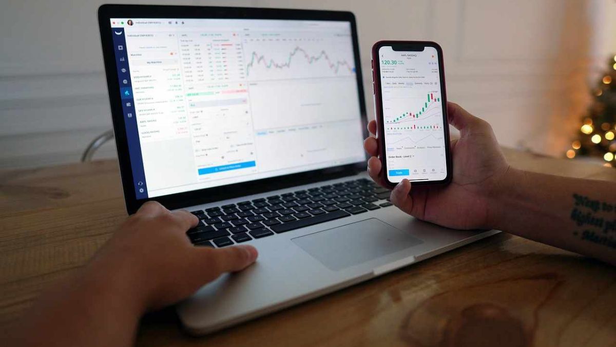A person engaged in trading using both a laptop and a mobile phone positioned on their desk