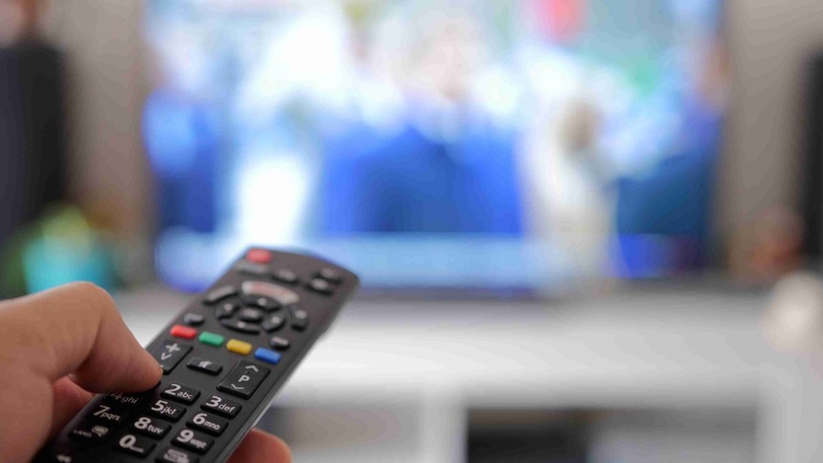 A person holding a remote control pointed toward a blurry flat-screen television