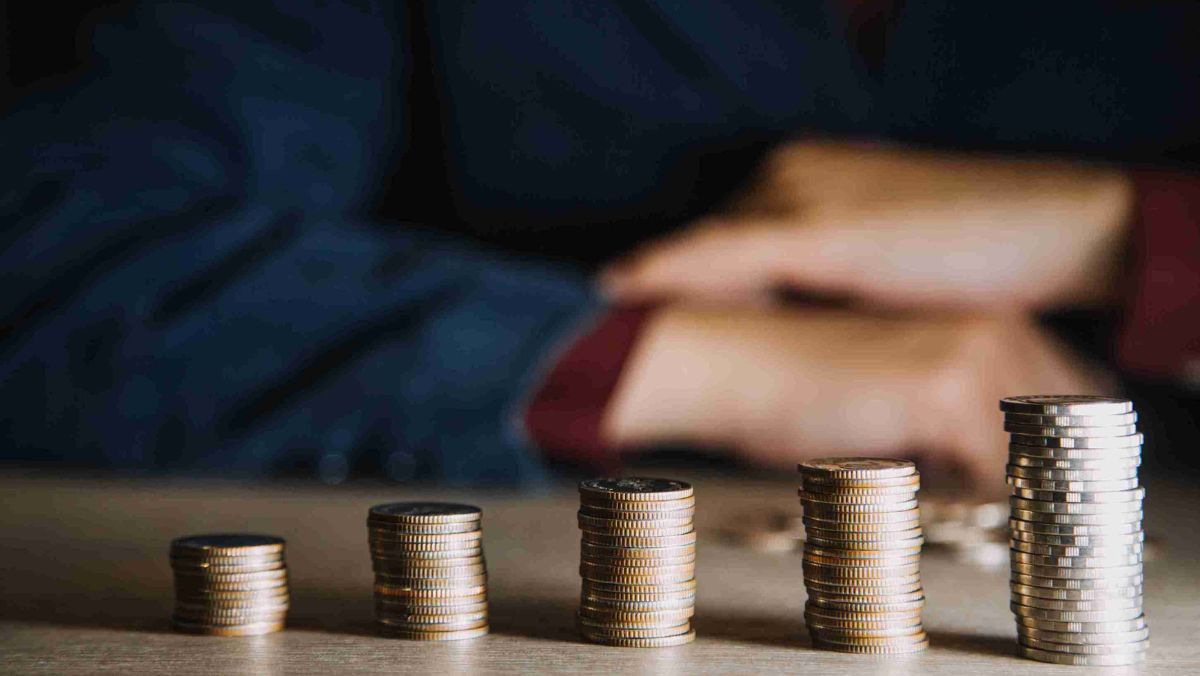 A person is framed against the backdrop of a mounting stack of coins