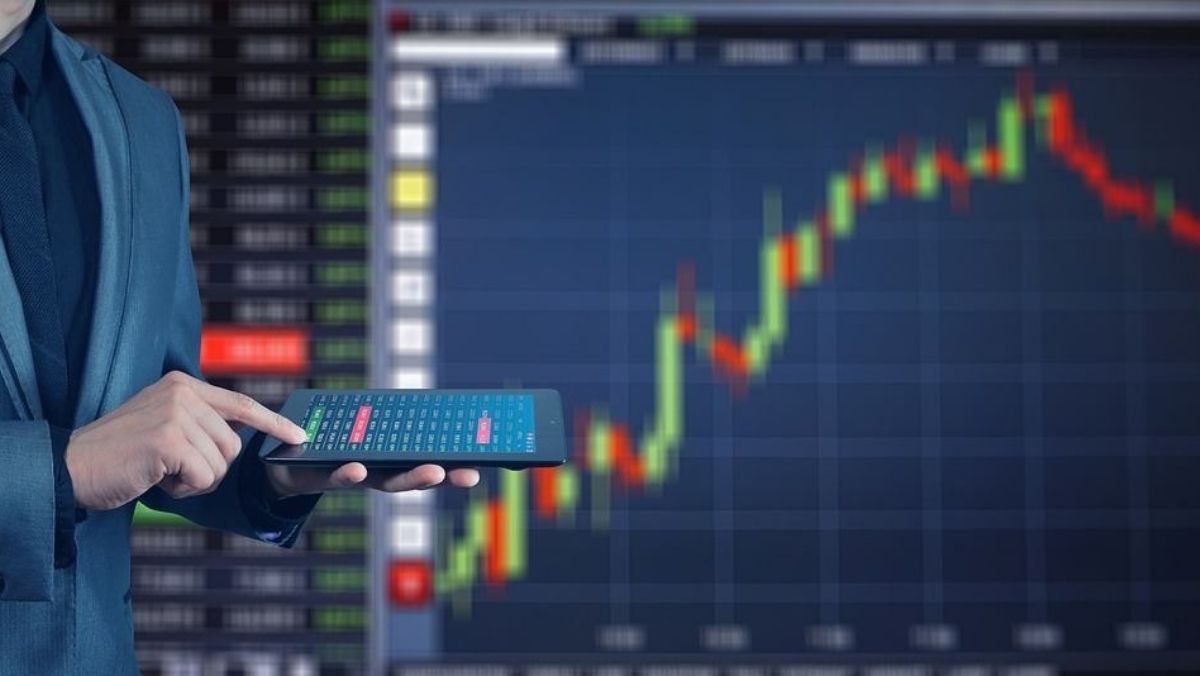 A person touching a tablet with a panoramic digital screen in the background, revealing a live trading chart