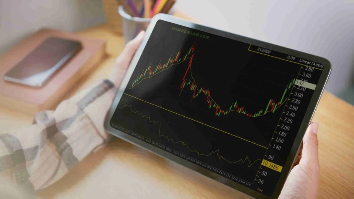 A person with a tablet displaying a live trading chart, set on the table