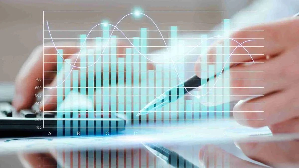 A person working behind the scenes, using a calculator and a pen, with a bar and line graph positioned in the foreground