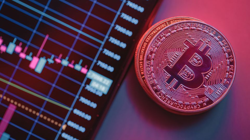 A red-hued Bitcoin token in front of a digital trading chart, highlighting cryptocurrency market analysis