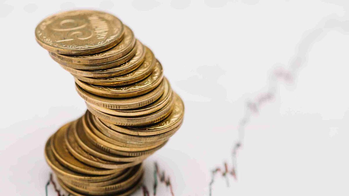 A stack of golden coins positioned beneath a line chart illustrating trading trends