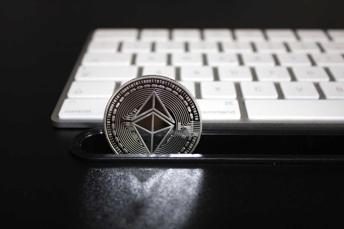 An Ethereum coin stands in front of a white keyboard on a dark desk