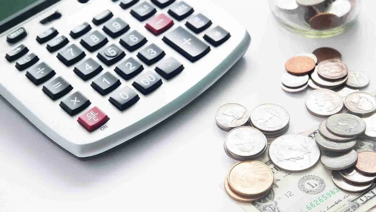 An arrangement of a calculator, paper currency, and coins spread out on a table