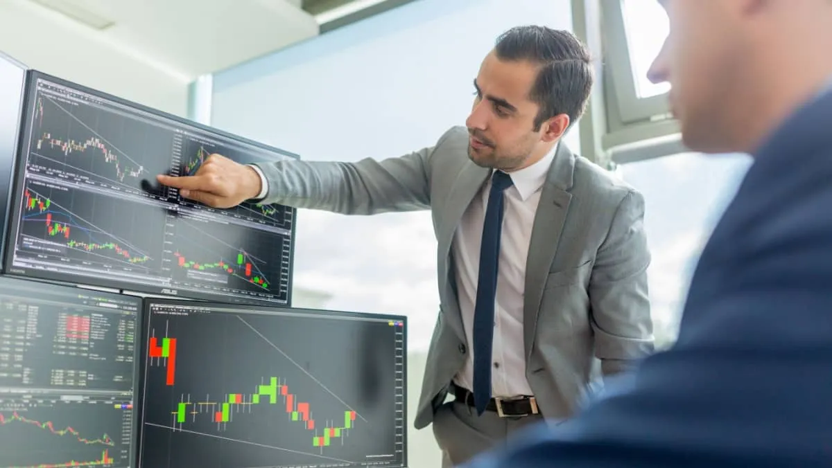 Businessmen engaged in stock trading, one pointing at the trading oscillator point on the screen while the other observes