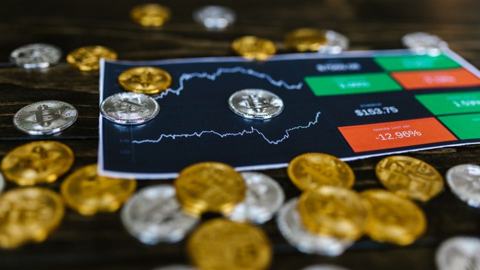 Cryptocurrency coins spread on a table with a digital tablet displaying live trading trends and graphs