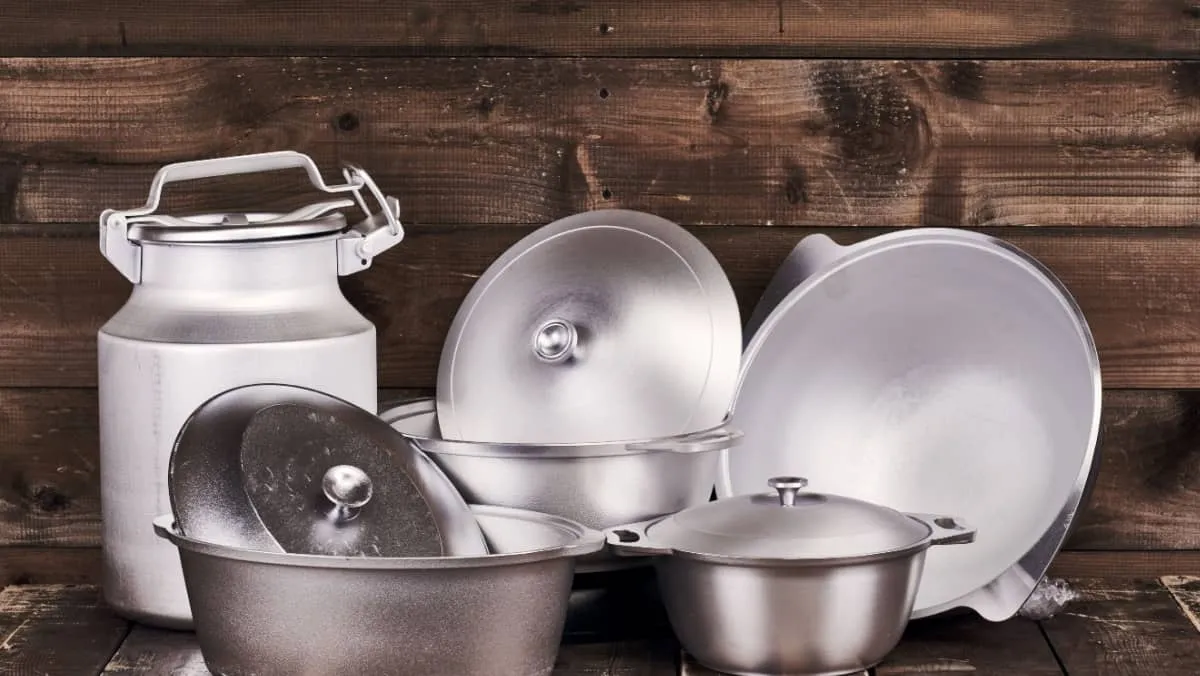 Different cast aluminium pots, pans and water-can on old grunge wooden table against wood wall background