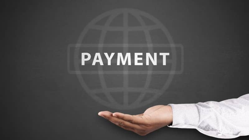 Hand presenting the word PAYMENT with a globe icon on a dark background