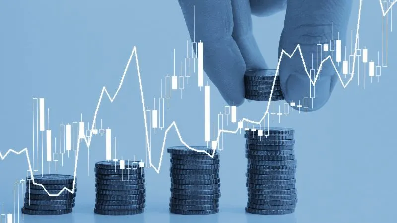 Hand stacking coins with stock market graph overlays, symbolizing investment growth.