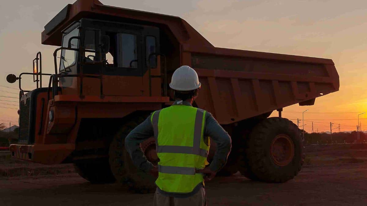 Man wearing a reflective vest and a hard helmet standing near a mining truck