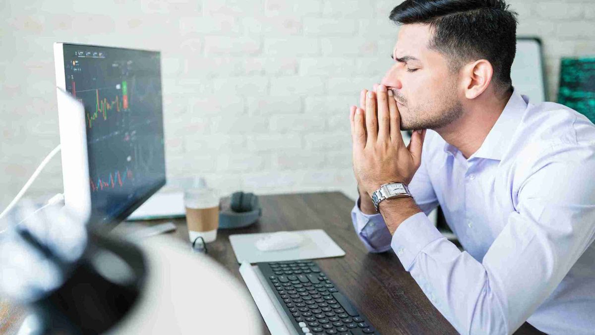 Person making a prayer-like hand gesture while facing a computer monitor