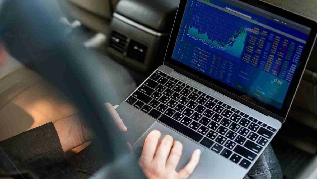 Positioned on a person's lap, a laptop is open, revealing a trading screen