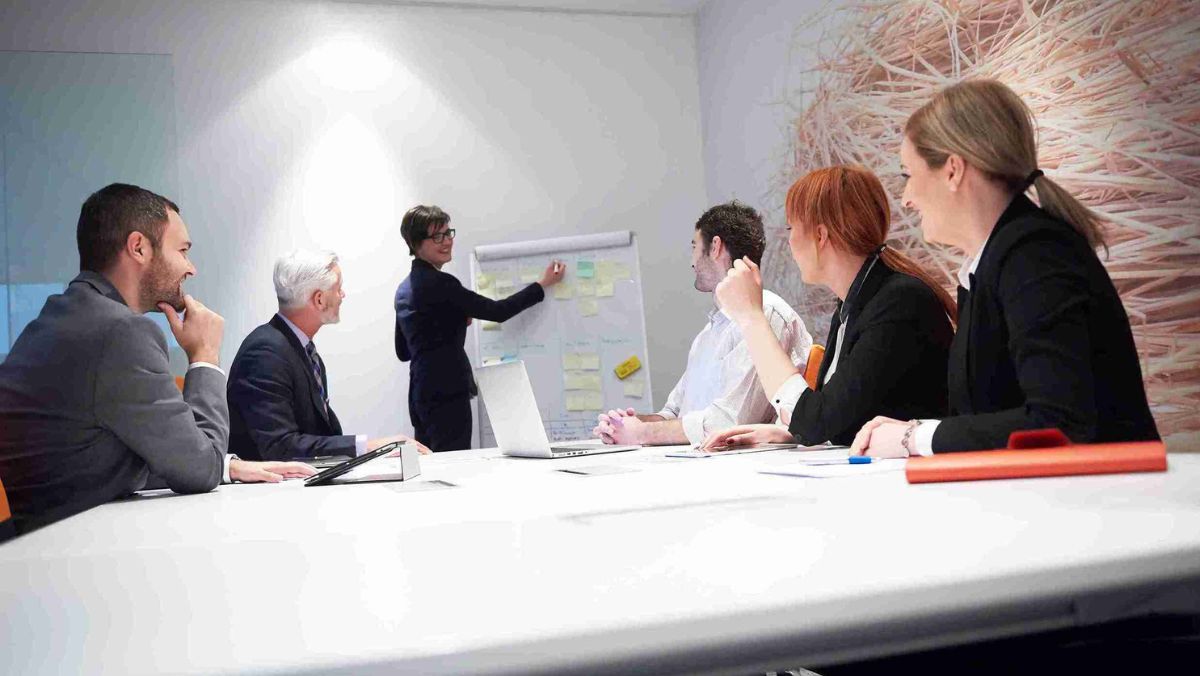 Professionals in a meeting engaged in discussions, with one person delivering a presentation