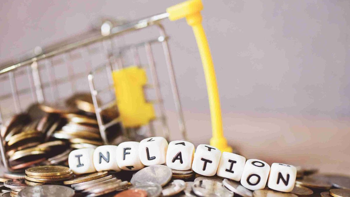 Scattered coins accompanied by a miniature shopping cart in the backdrop with dice arranged to spell out the word INFLATION