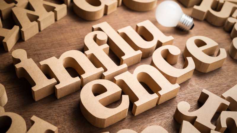 The image displays the word influence in bold wooden letters with a lightbulb placed on the right side