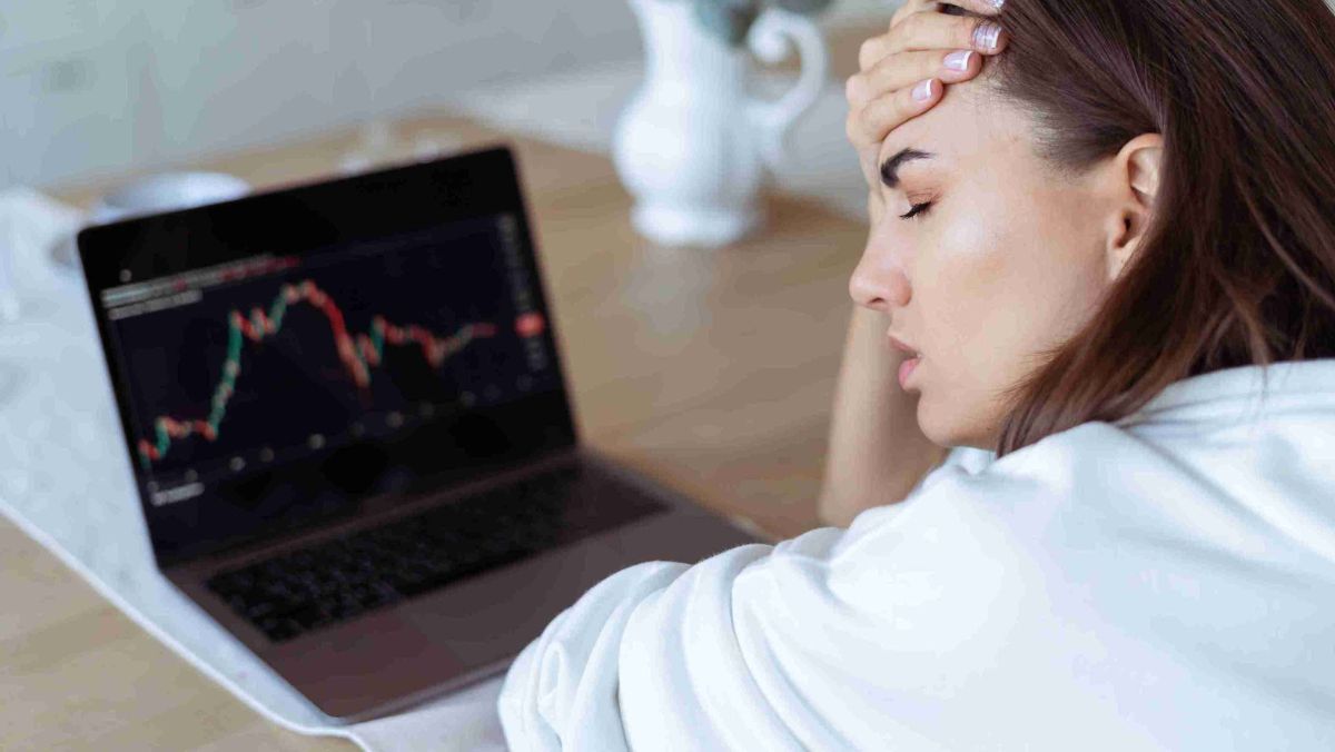 The woman's face reveals signs of stress as she works on her laptop at the table