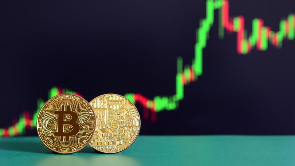 Two Bitcoin tokens against the backdrop of a green upward trending financial chart, representing the rise in cryptocurrency value