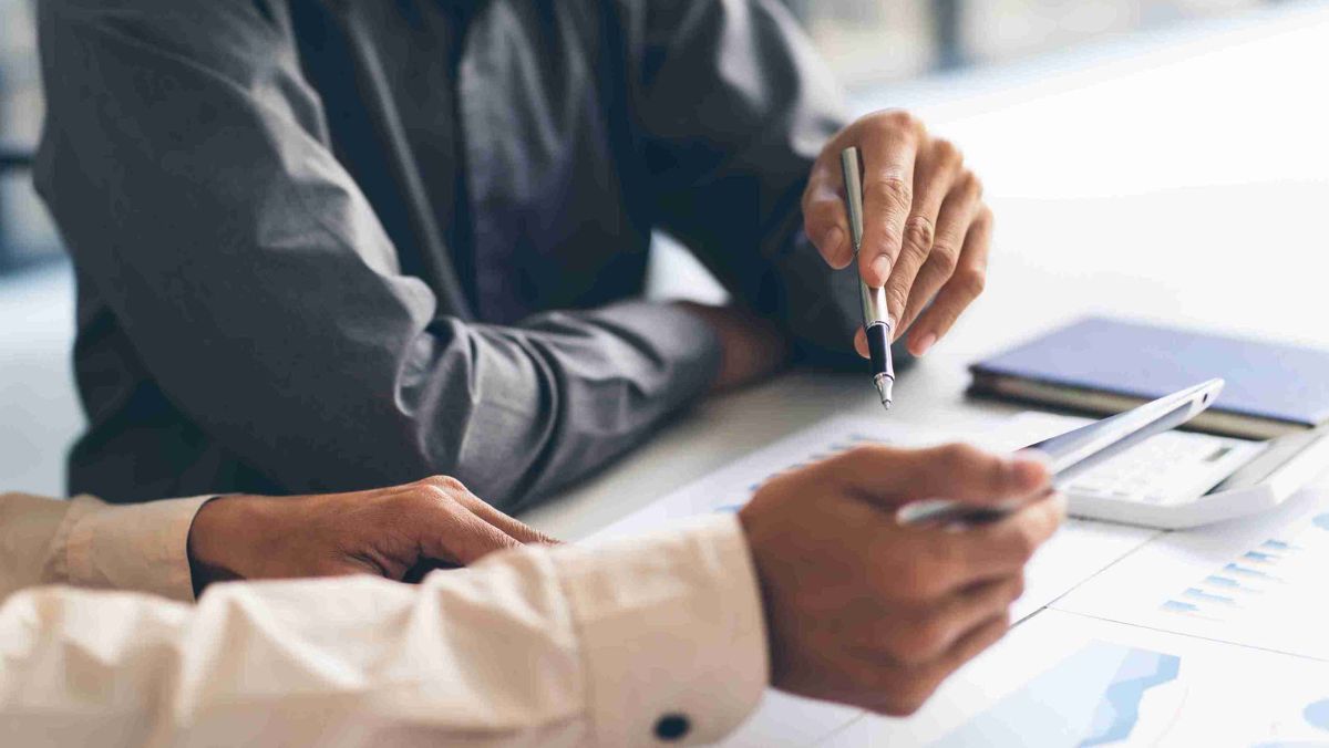 Two people engage in a conversation, with one person holding a pen while the other has a document placed on the desk