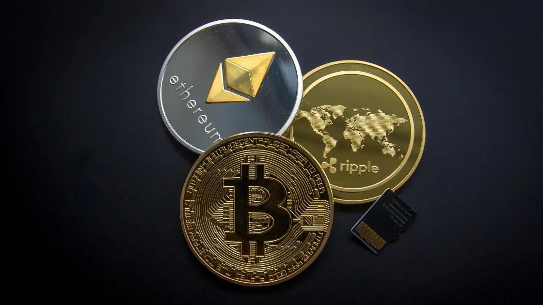 Various cryptocurrency coins including Bitcoin Ethereum and Ripple arranged next to a microSD card on a dark surface symbolizing the digital storage of virtual currencies