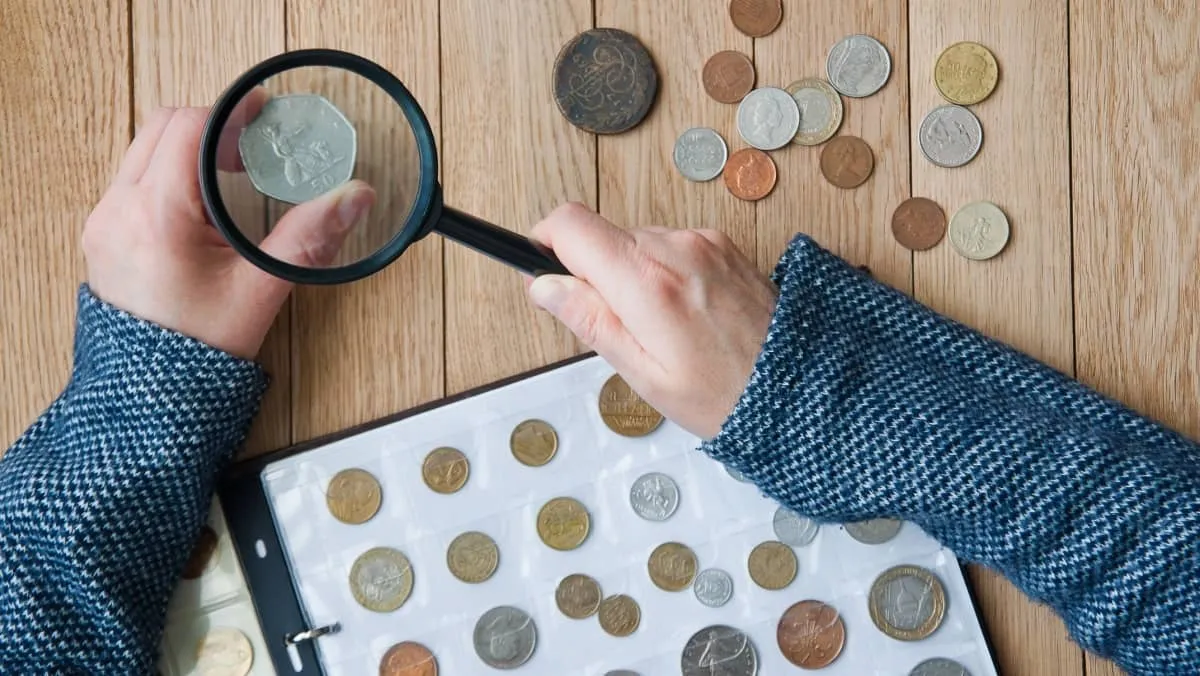 Woman-numismatist views coins from a coin album through a magnifying glass. Top view.