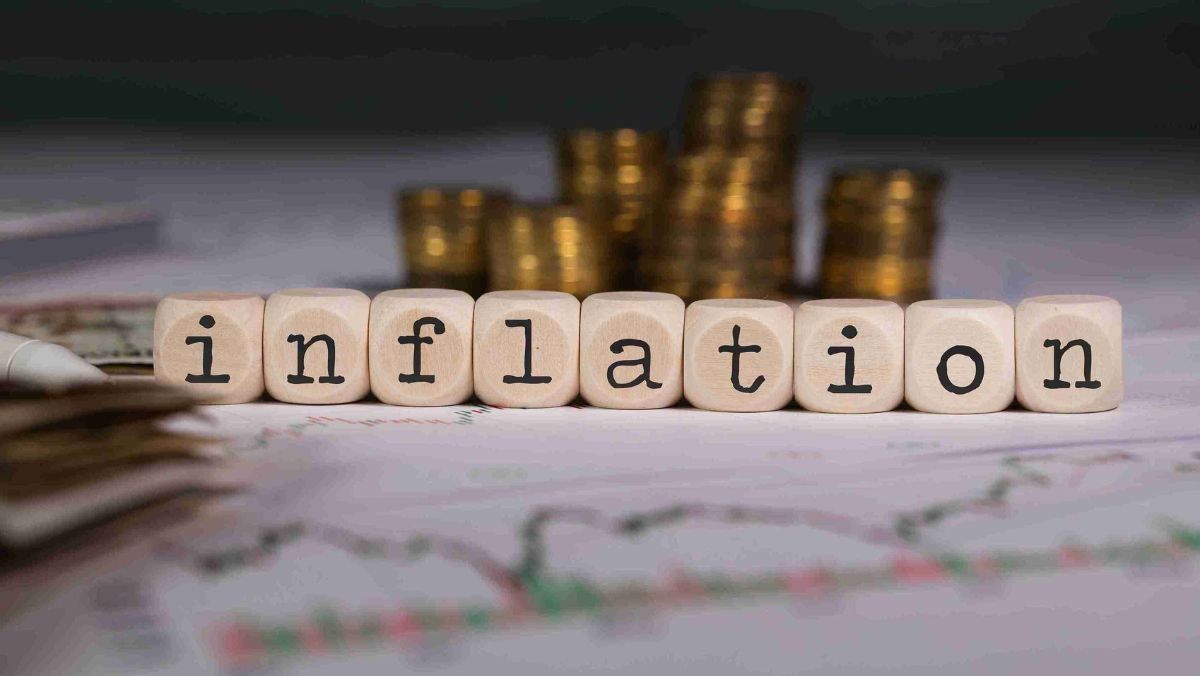 Wooden dice displaying the term INFLATION accompanied by a stack of gold coins in the background