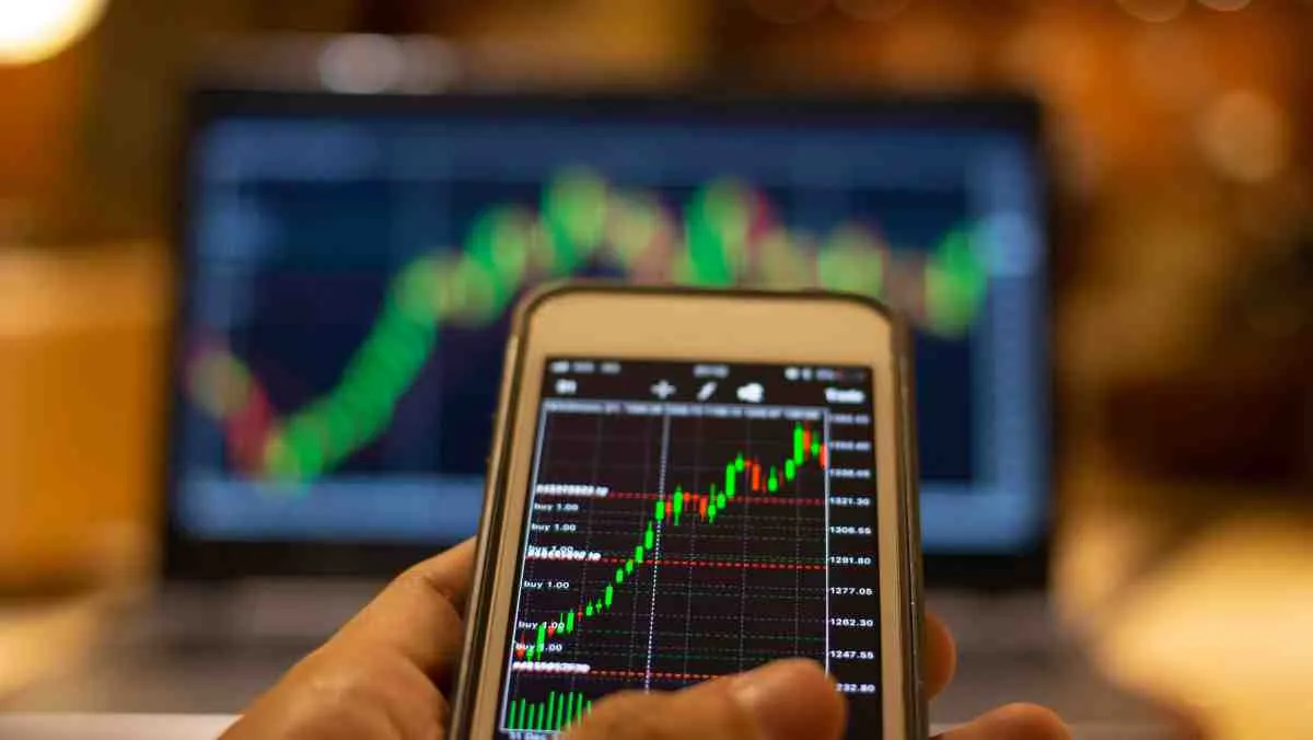 a-hand-with-a-smartphone-used-for-social-trading-with-a-background-of-a-blurry-laptop-screen.width-1200.format-jpg.jpg